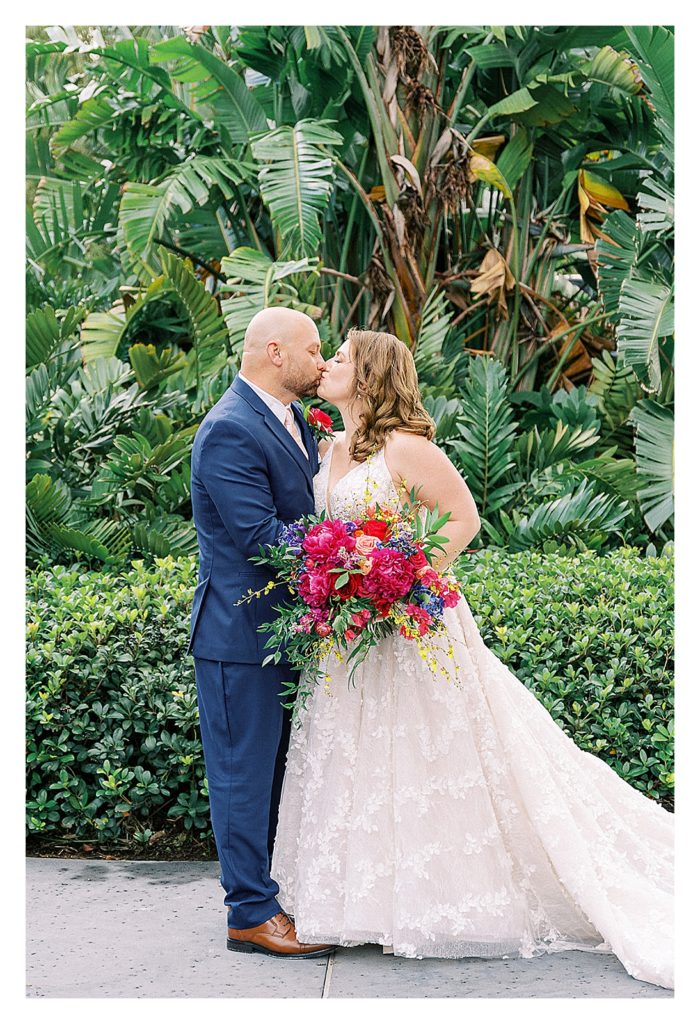 bride and groom kiss at Disney Polynesian Resort. Bride carries a magenta bouquet of peonies. 